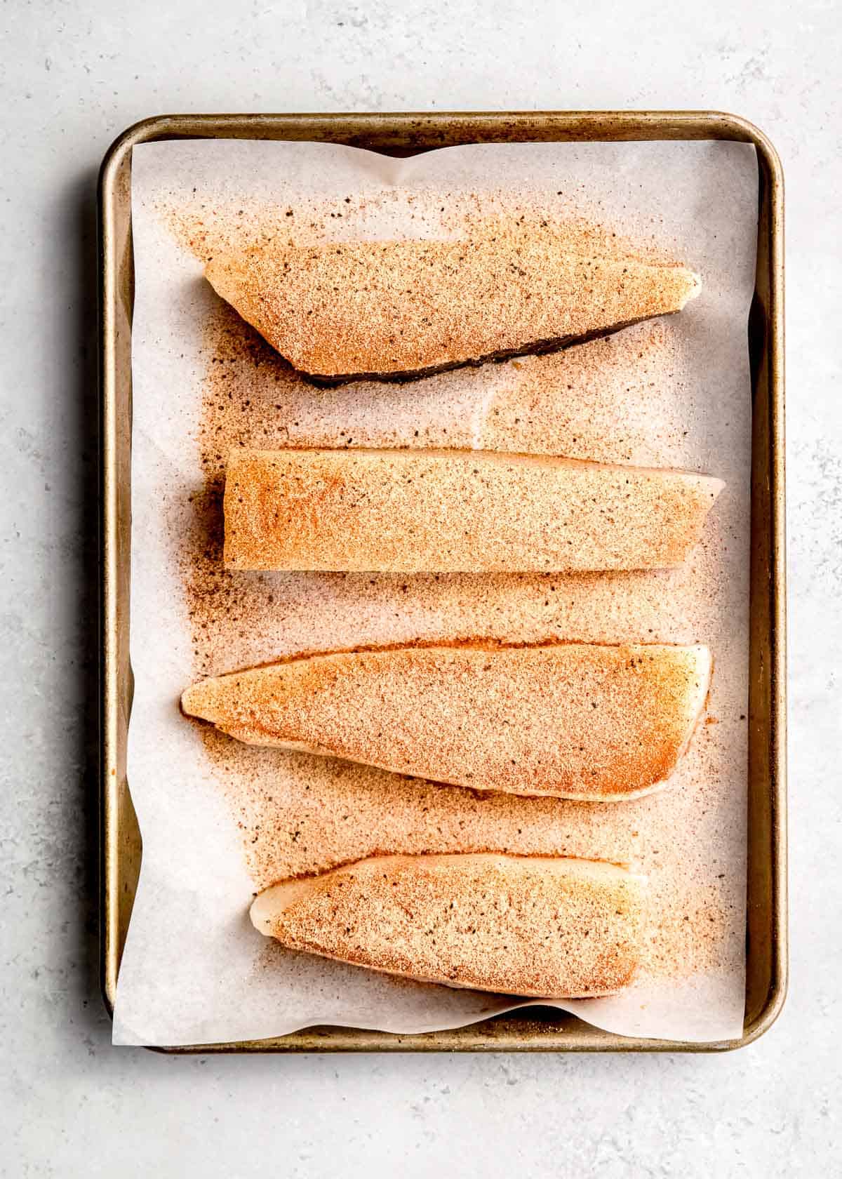 seasoning being added to halibut filets on baking sheet