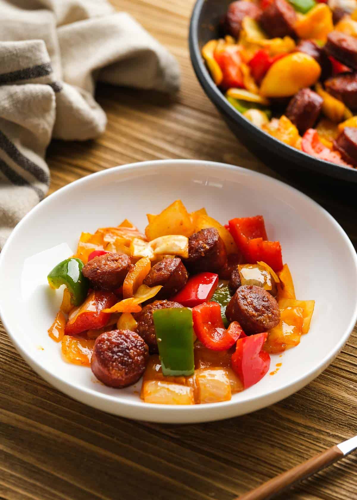 sausage and peppers with cabbage in white bowl on wooden table