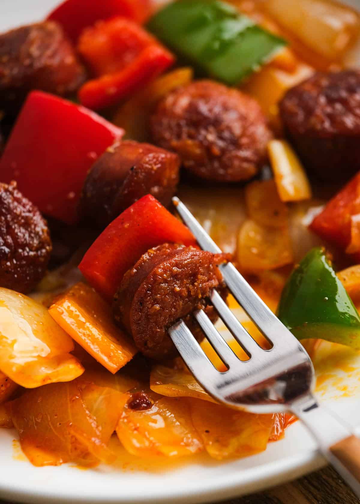 bite of sausage and peppers with cabbage on a fork with white bowl in background