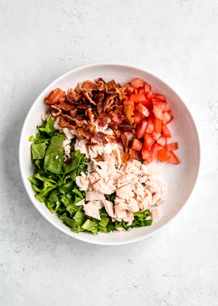 tomatoes and bacon being added to white bowl