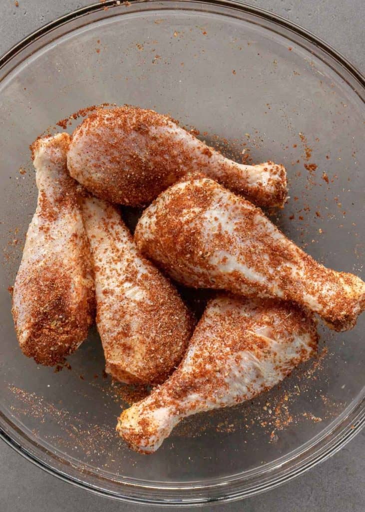 chicken legs covered in seasonings in a glass bowl