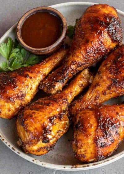 a plate with five bbq chicken legs and a ramekin of bbq sauce