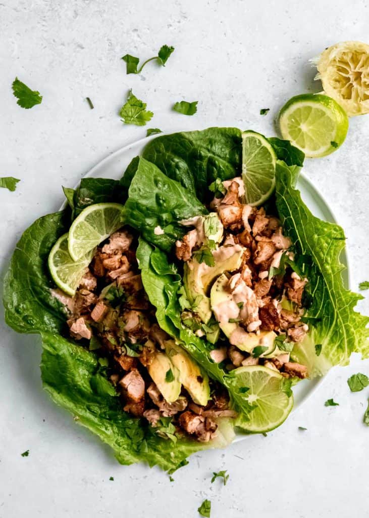 overhead view of two chipotle chicken taco lettuce wraps with lime, fresh herbs, and chipotle sauce