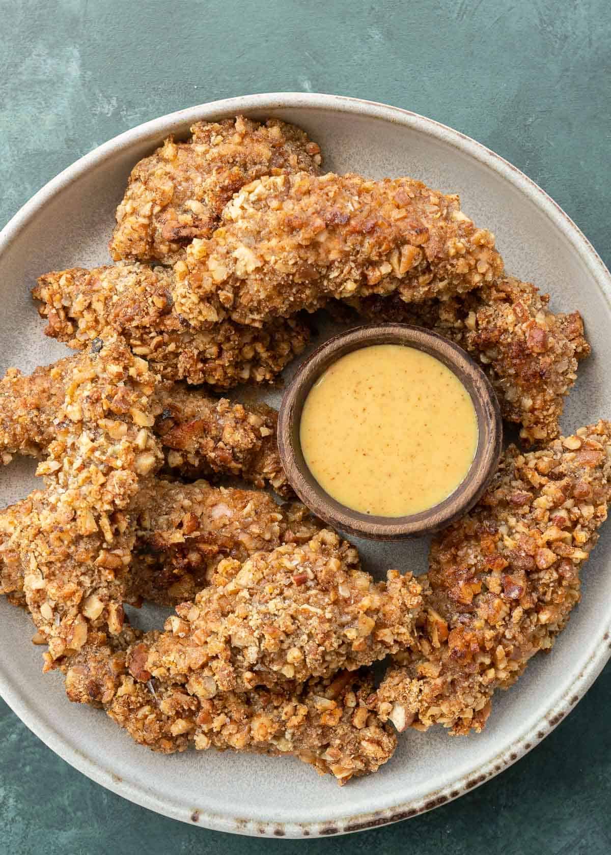 overhead view of a platter of pecan-crusted keto chicken tenders around sugar-free honey mustard sauce