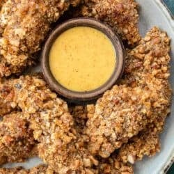 an overhead shot of a batch of crispy pecan crusted chicken surrounding a ramekin of sugar-free honey mustard