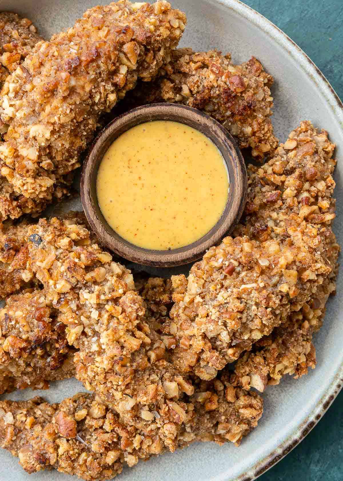 an overhead shot of a batch of crispy pecan crusted chicken surrounding a ramekin of sugar-free honey mustard