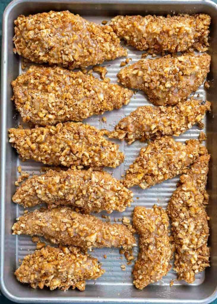 twelve pecan crusted chicken strips on a baking sheet