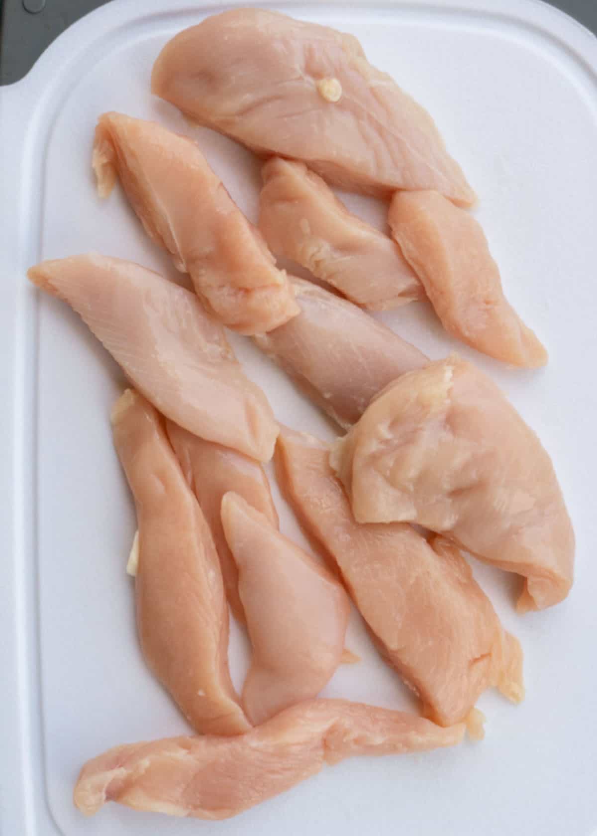 strips of chicken cut from chicken breasts on a white cutting board