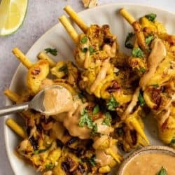 a spoon full of peanut sauce drizzling the flavorful sauce all over chicken satay skewers