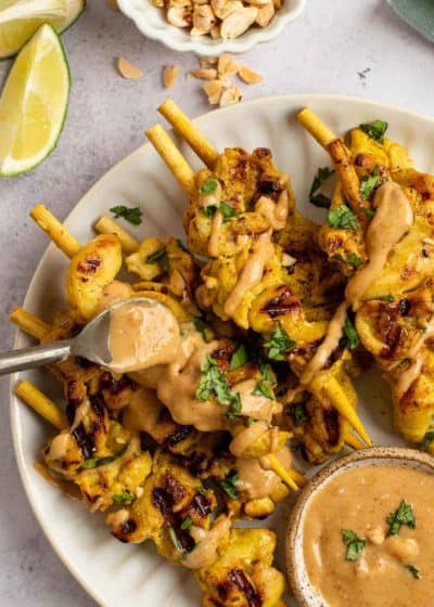 a spoon full of peanut sauce drizzling the flavorful sauce all over chicken satay skewers