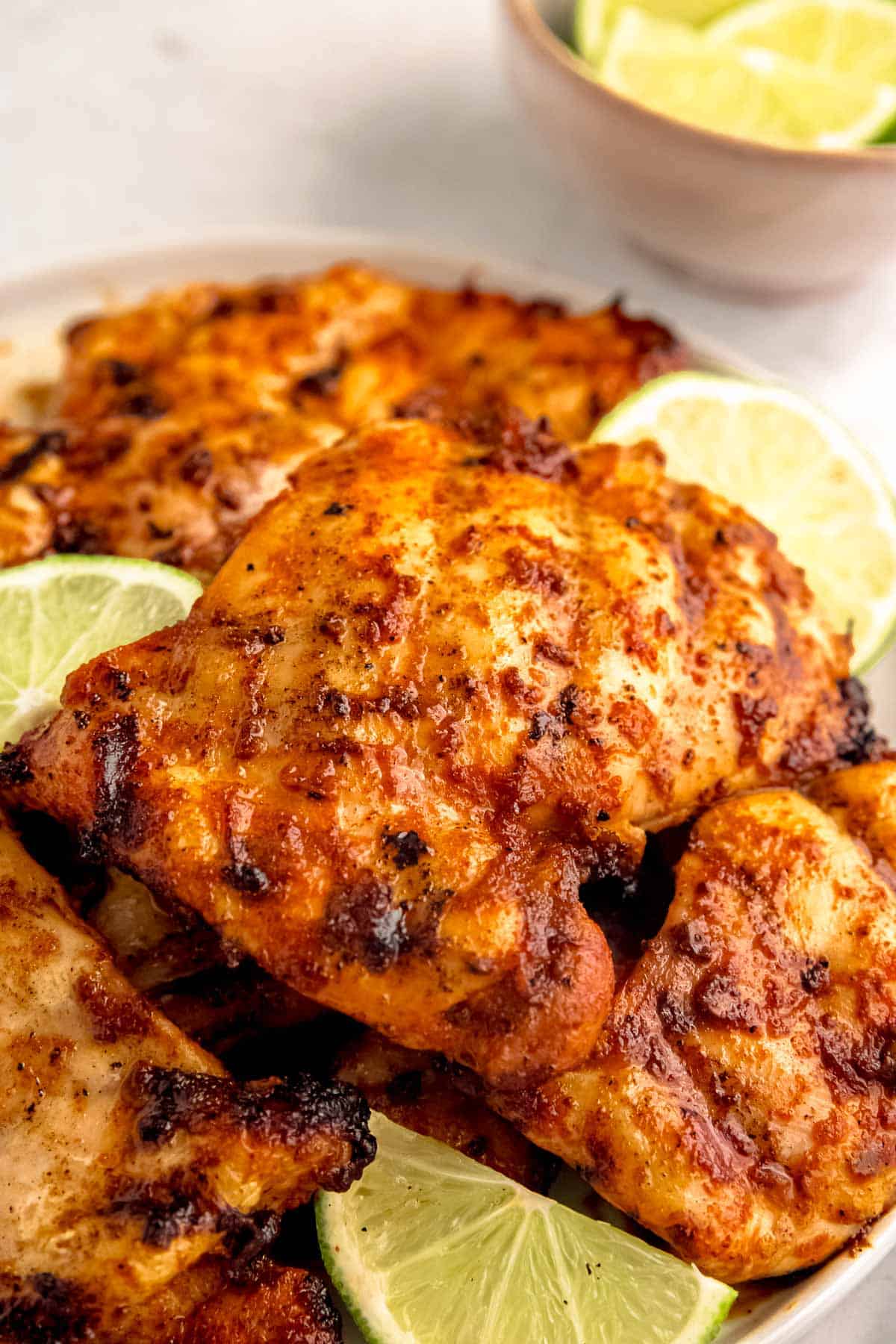easy grilled chipotle chicken thighs stacked on a white plate surrounded by lime wedges