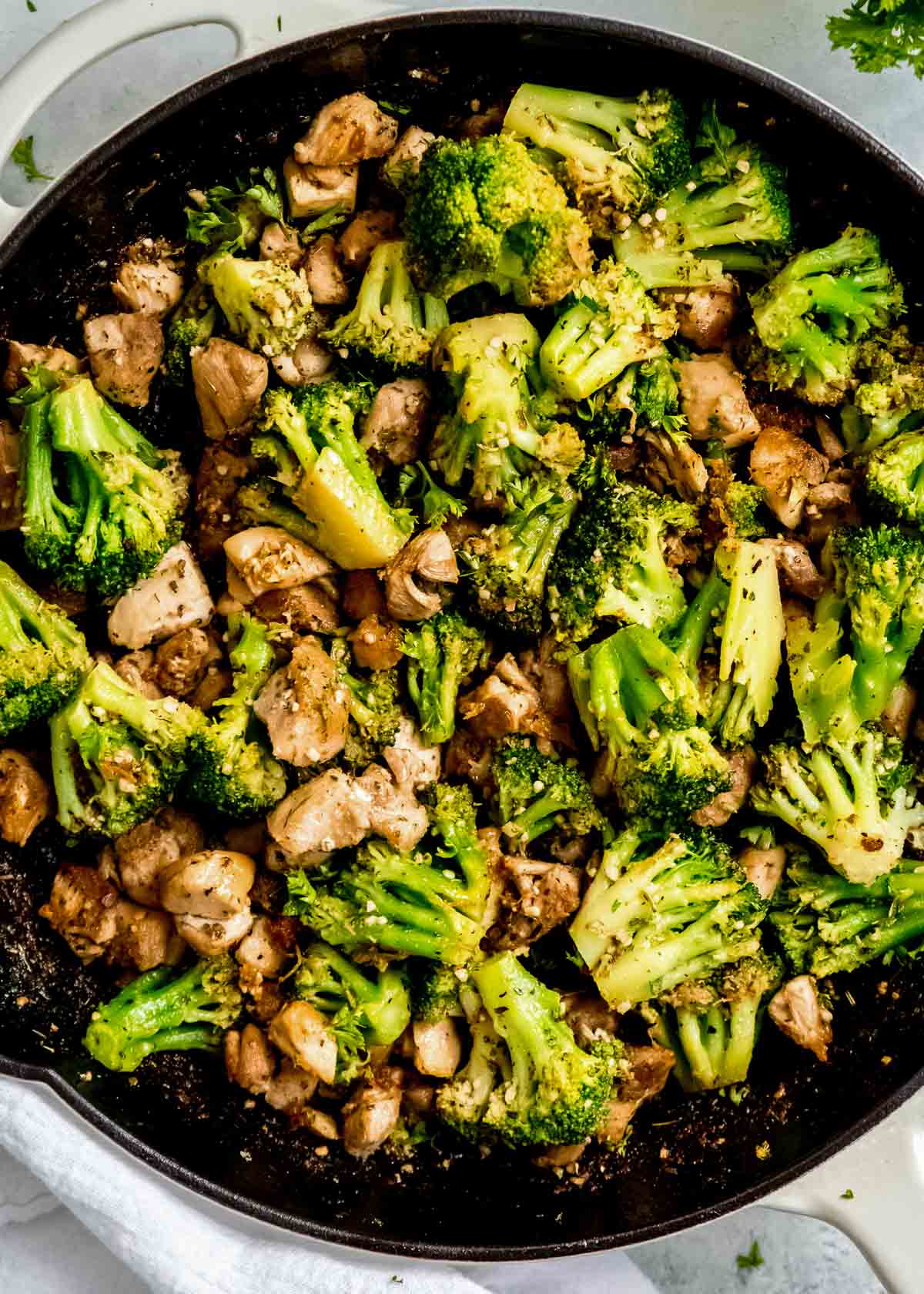 closeup overhead shot of garlic butter sauce coating juicy chicken thigh bites and frozen broccoli florets