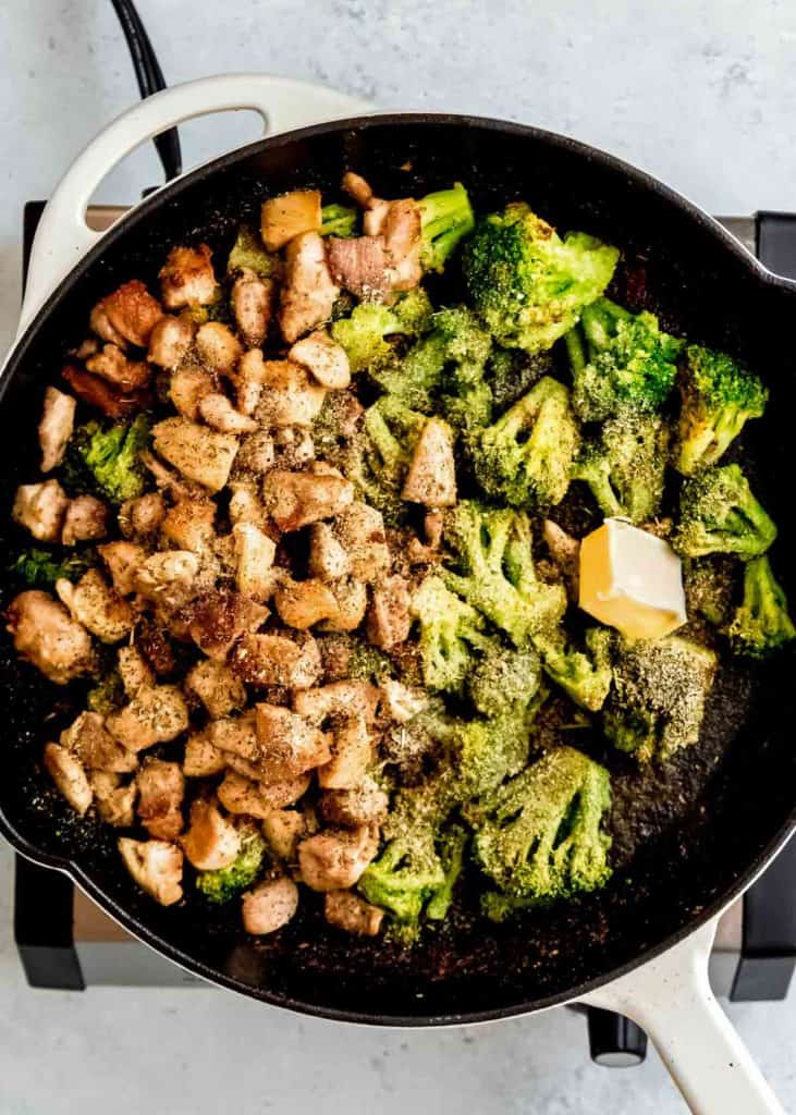 chicken thighs on one side of the skillet, broccoli florets on the other side of the skillet. Both sides are sprinkled with seasonings, red wine vinegar, butter, and garlic.