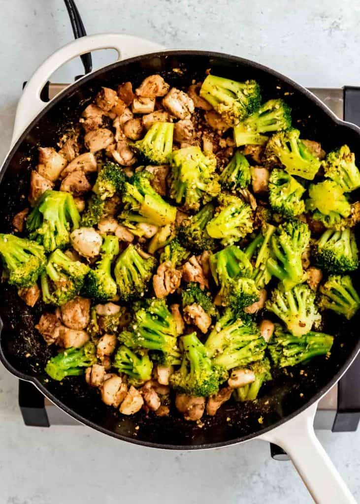 chicken thighs and broccoli cooking in a garlic butter sauce in a skillet