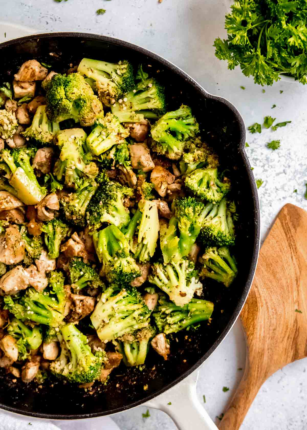 overhead view of garlic butter chicken and broccoli skillet sprinkled with fresh herbs in a skillet beside a wooden spoon