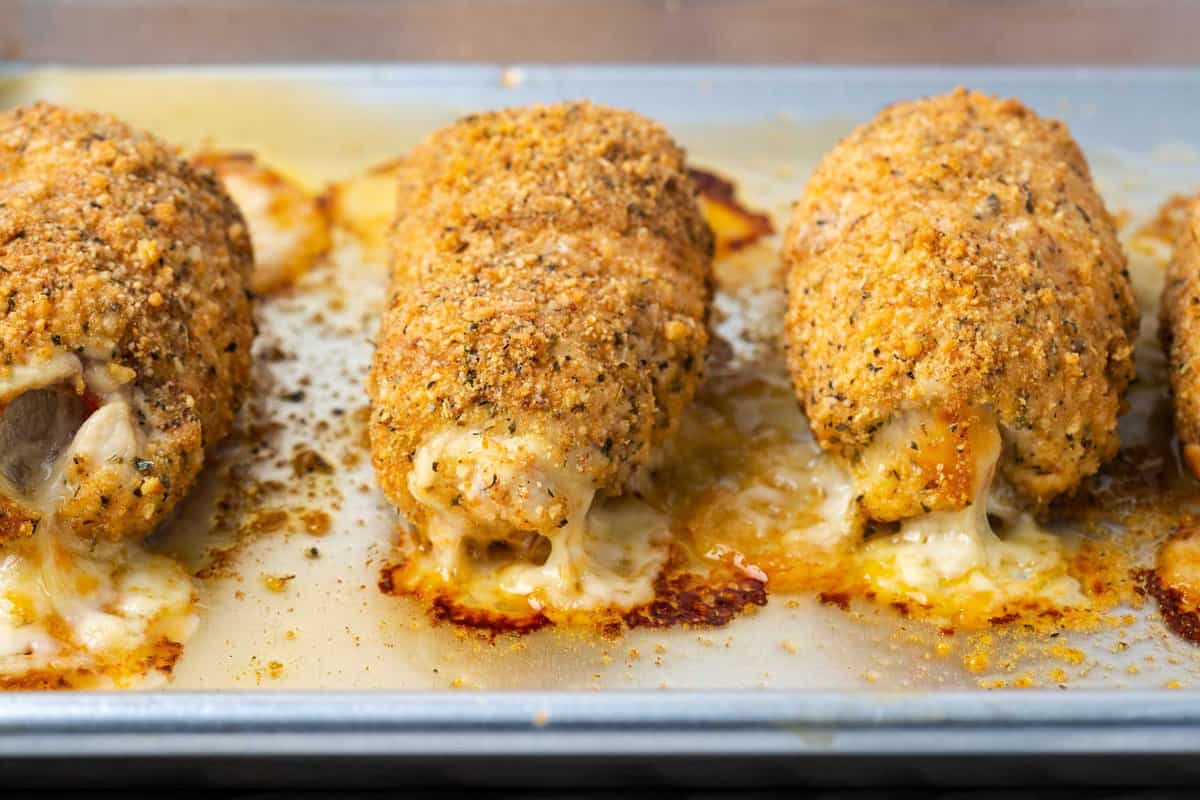 a horizontal image showing four baked stuffed chickens with mozzarella oozing out of the sides