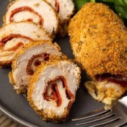 slices of juicy pepperoni stuffed chicken beside a whole breaded stuffed chicken breast on a black plate with a salad on the side