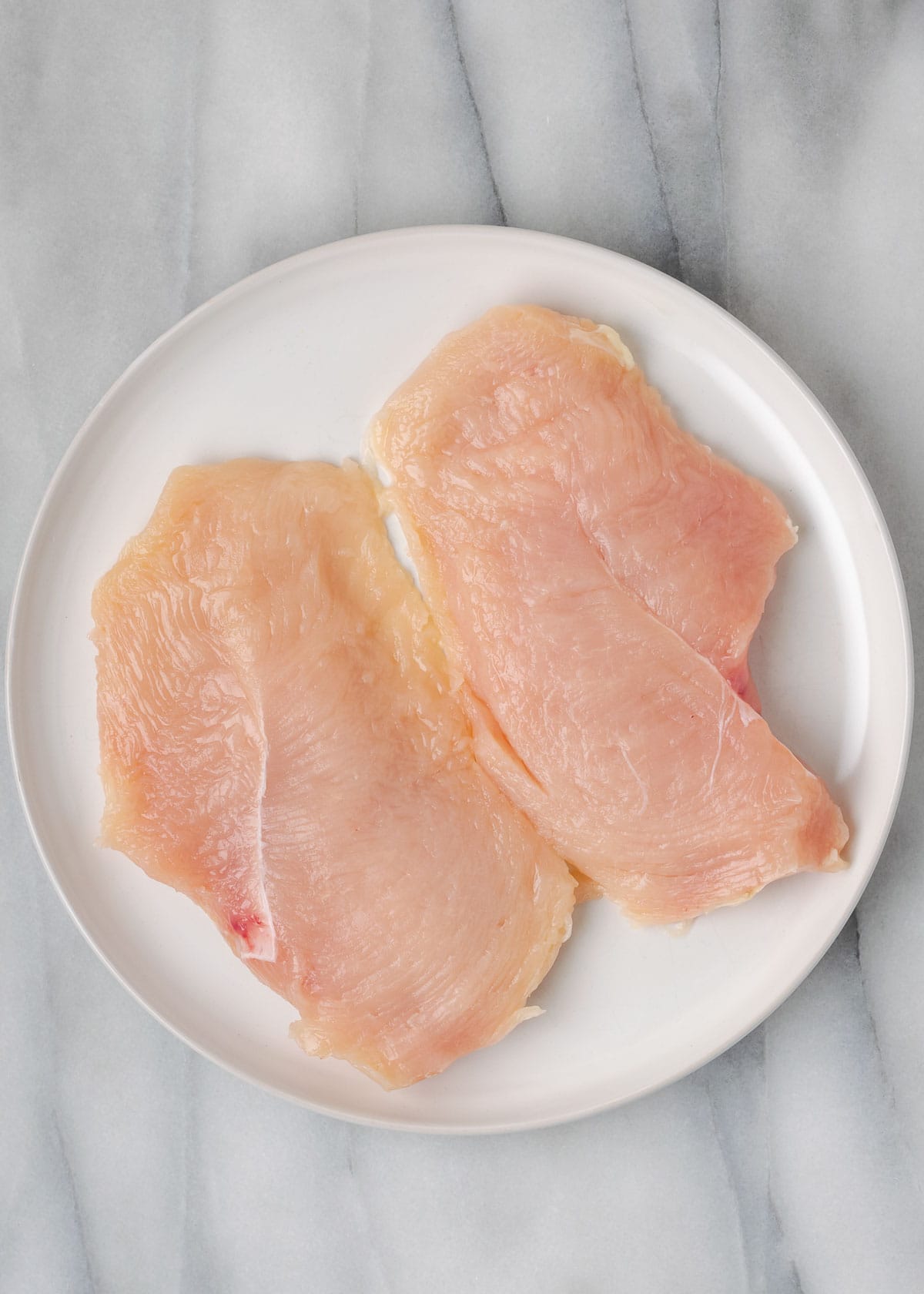 a large chicken breast sliced in half horizontally and pounded thin on a white plate