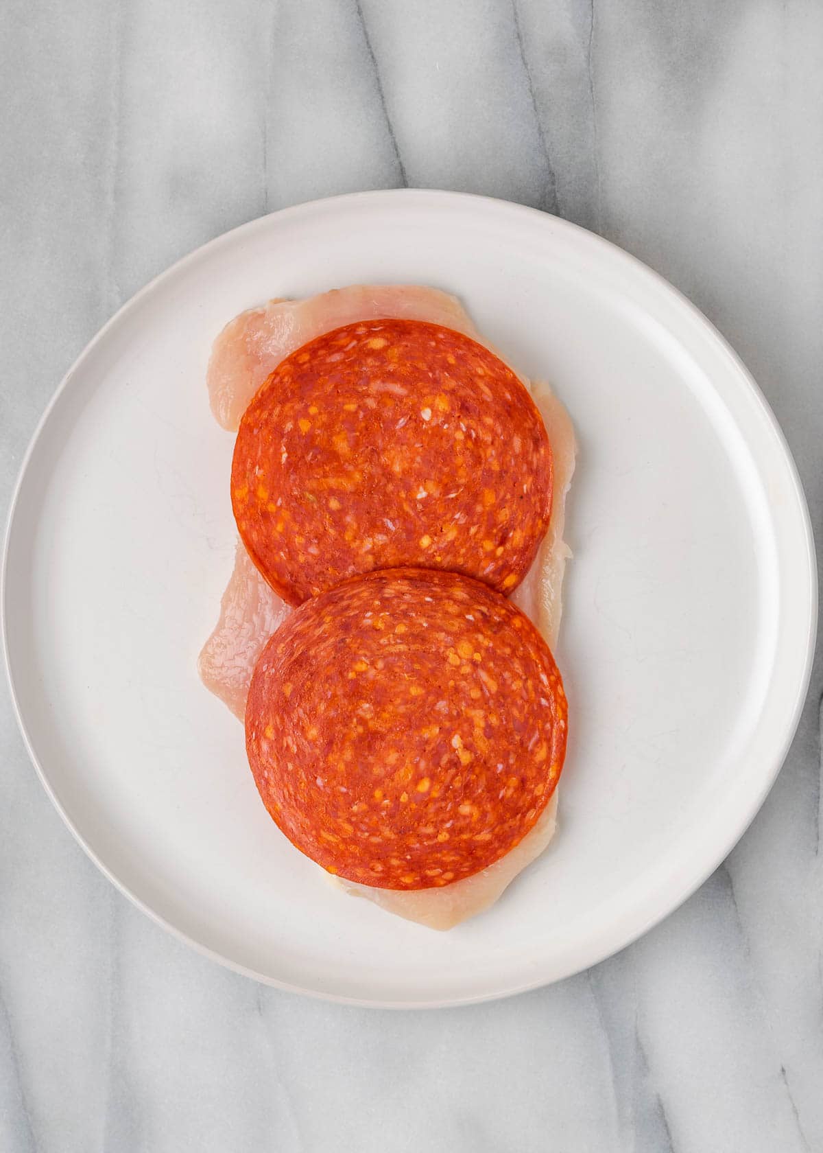 large slices of pepperoni on a flattened chicken cutlet