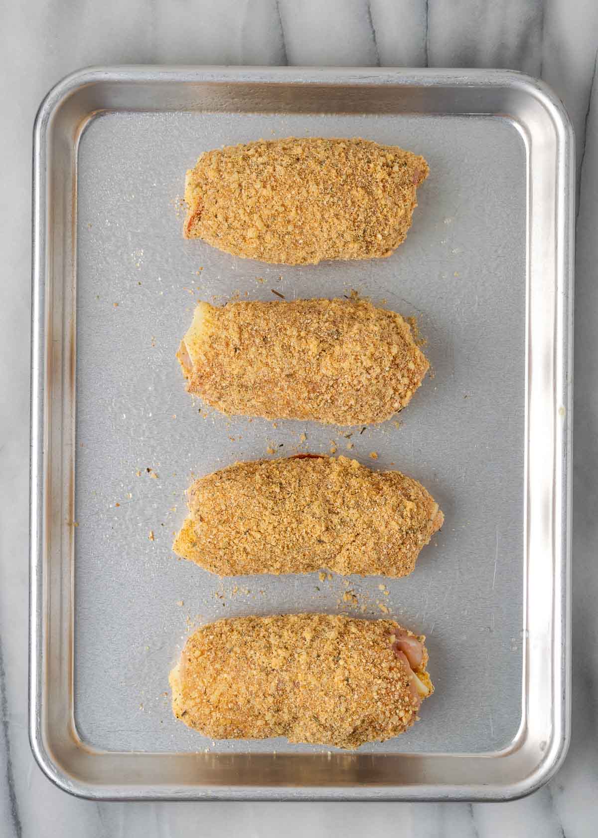 four breaded stuffed chicken pieces on a baking sheet