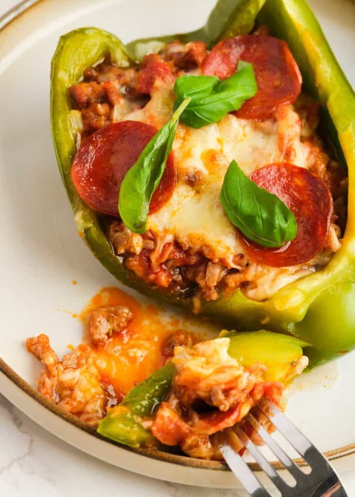 a fork taking a big bite of a keto pizza stuffed pepper with sausage and pepperoni filling