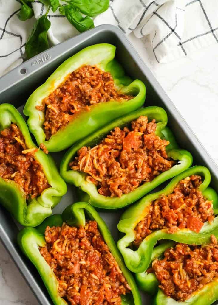 halved peppers filled with a sausage and pepperoni pizza mixture in a baking dish