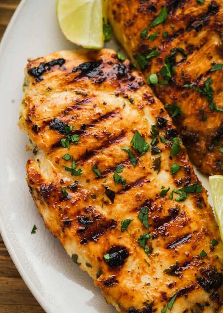 closeup view of juicy cilantro lime chicken with tasty grill marks and lime wedges on a white plate