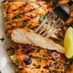 a white platter full of cilantro lime chicken; a fork showing a juicy slice