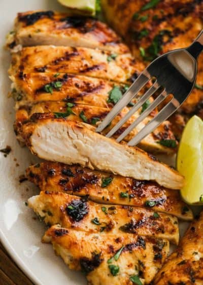a white platter full of cilantro lime chicken; a fork showing a juicy slice
