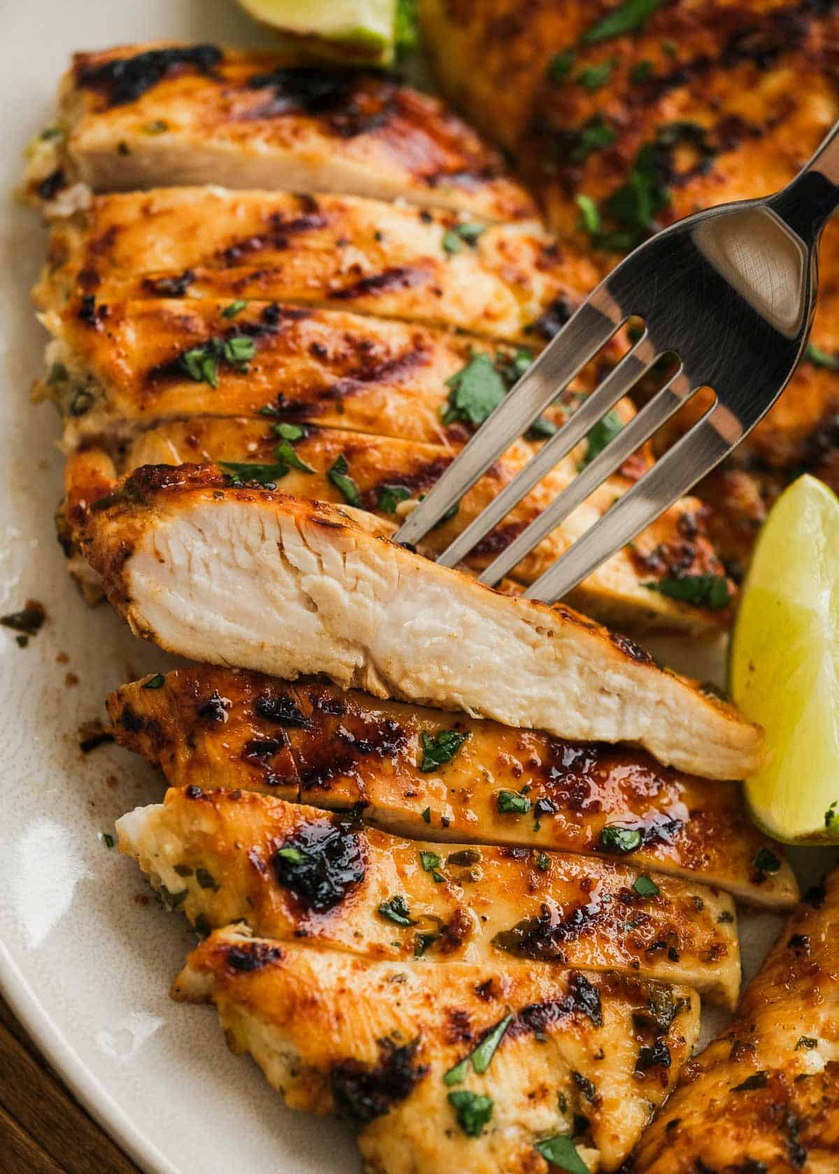 a white platter full of cilantro lime chicken; a fork showing a juicy slice
