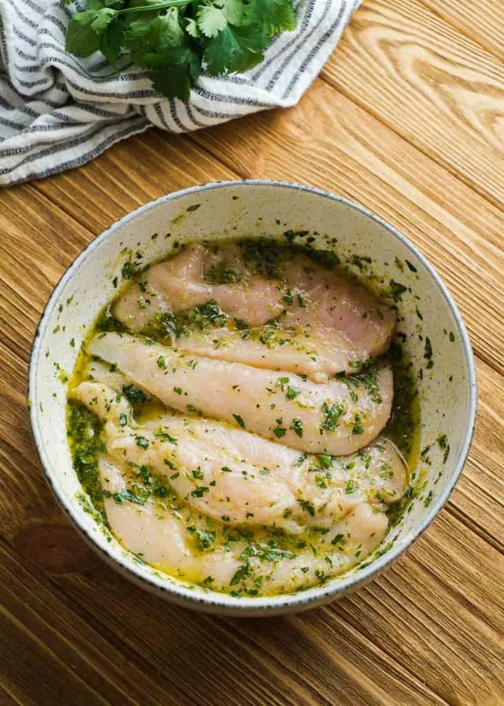 thin chicken breast cutlets in a white bowl full of cilantro lime marinade