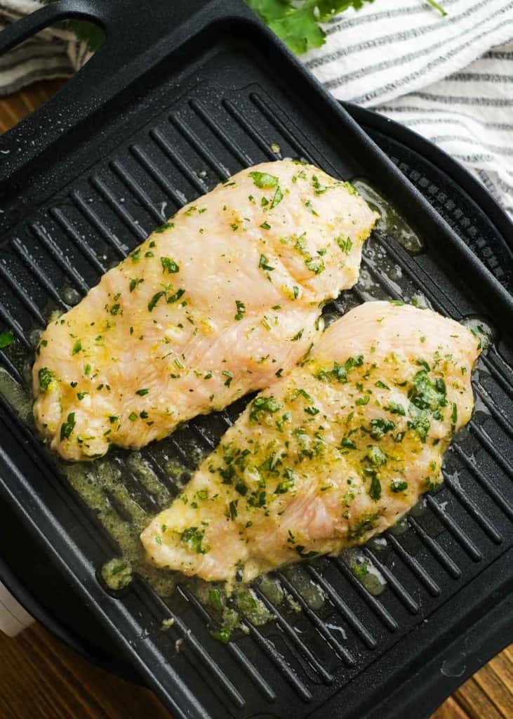 two marinated chicken breasts on a grill pan