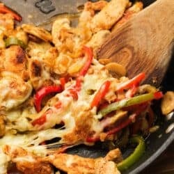 chicken cheesesteak skillet being removed from cast iron skillet with wooden spoon