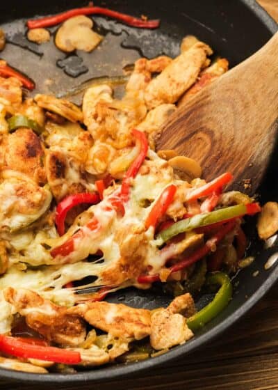 chicken cheesesteak skillet being removed from cast iron skillet with wooden spoon