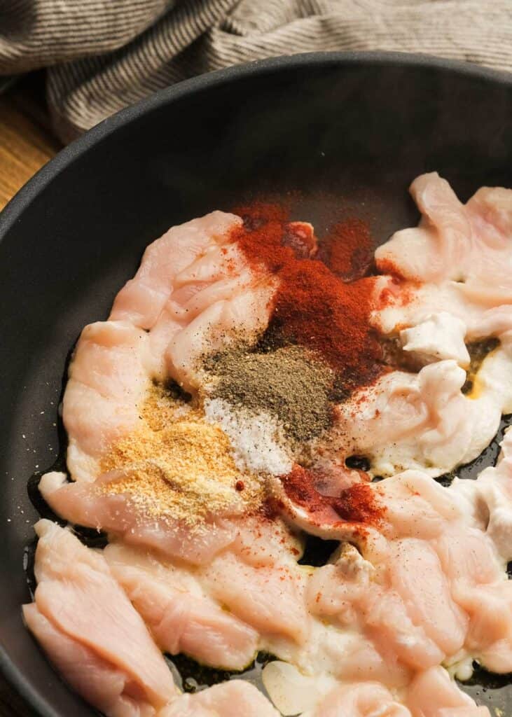 raw chicken and spices in a cast iron skillet