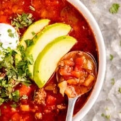 overhead image of taco soup in white bowl on silver platter with silver spoon