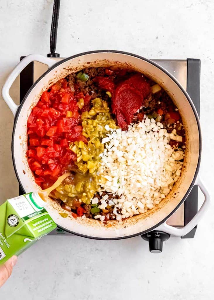 beef broth and remainin ingredients being added to taco soup in dutch oven