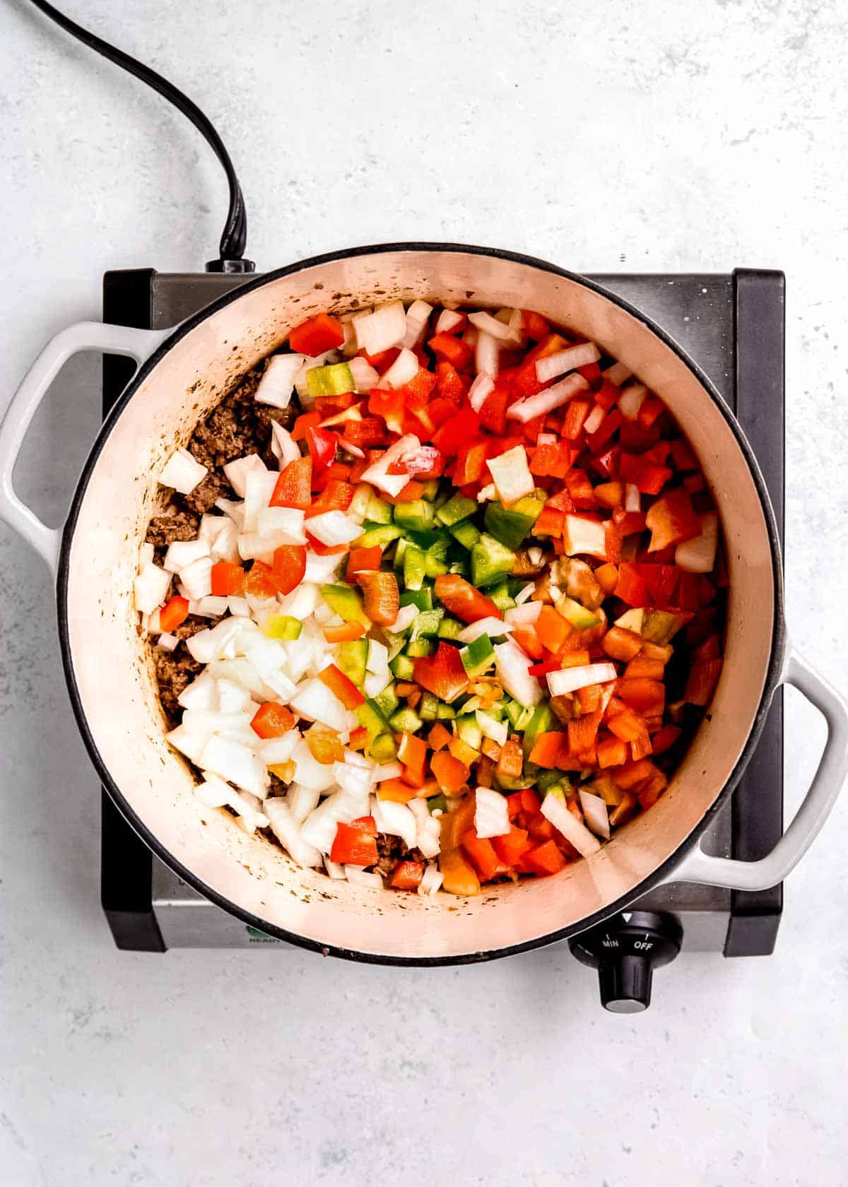 vegetables being added to dutch oven with ground beef