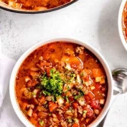 overhead image of stuffed pepper soup in white bowl with spoon on white table in background