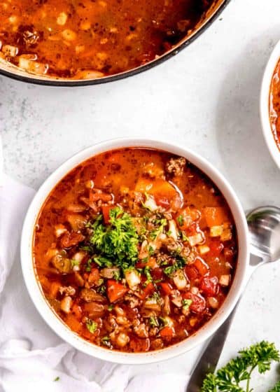 overhead image of stuffed pepper soup in white bowl with spoon on white table in background