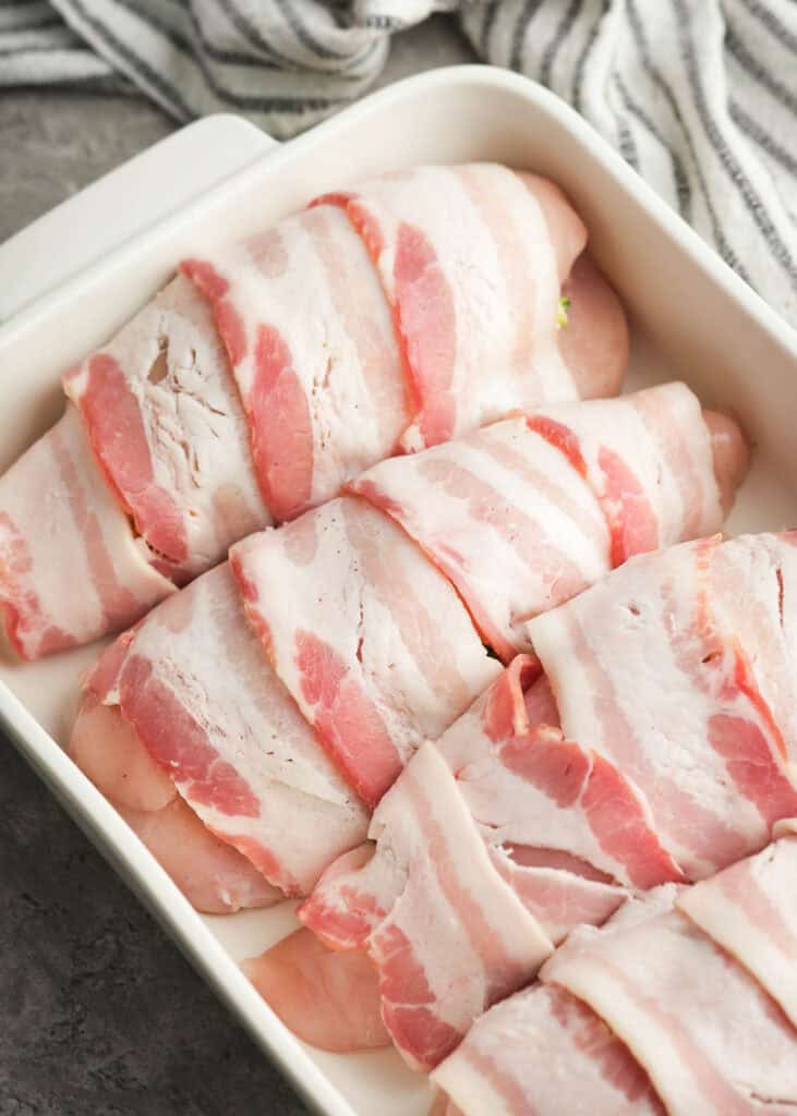 bacon wrapped stuffed chicken breasts in a white baking dish