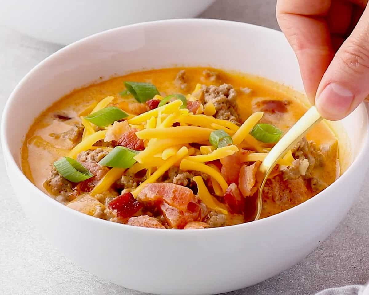 a spoonful of cheeseburger soup being removed from white bowl