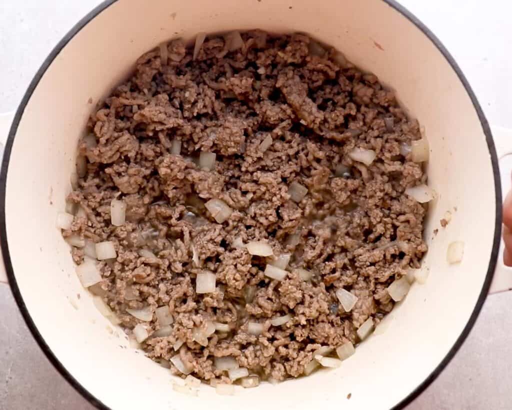 ground beef and onions being cooked in dutch oven