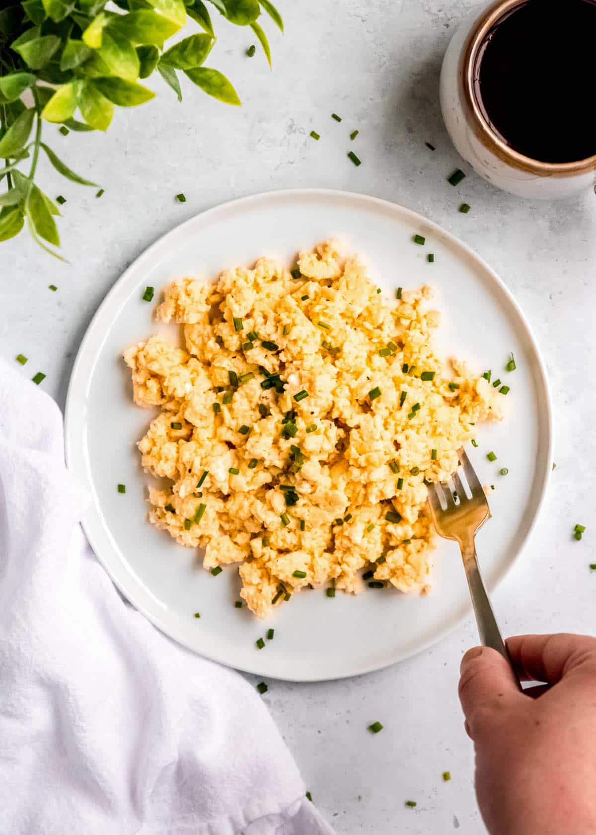 high protein scrambled eggs on a white plate with a cup of coffee on the side