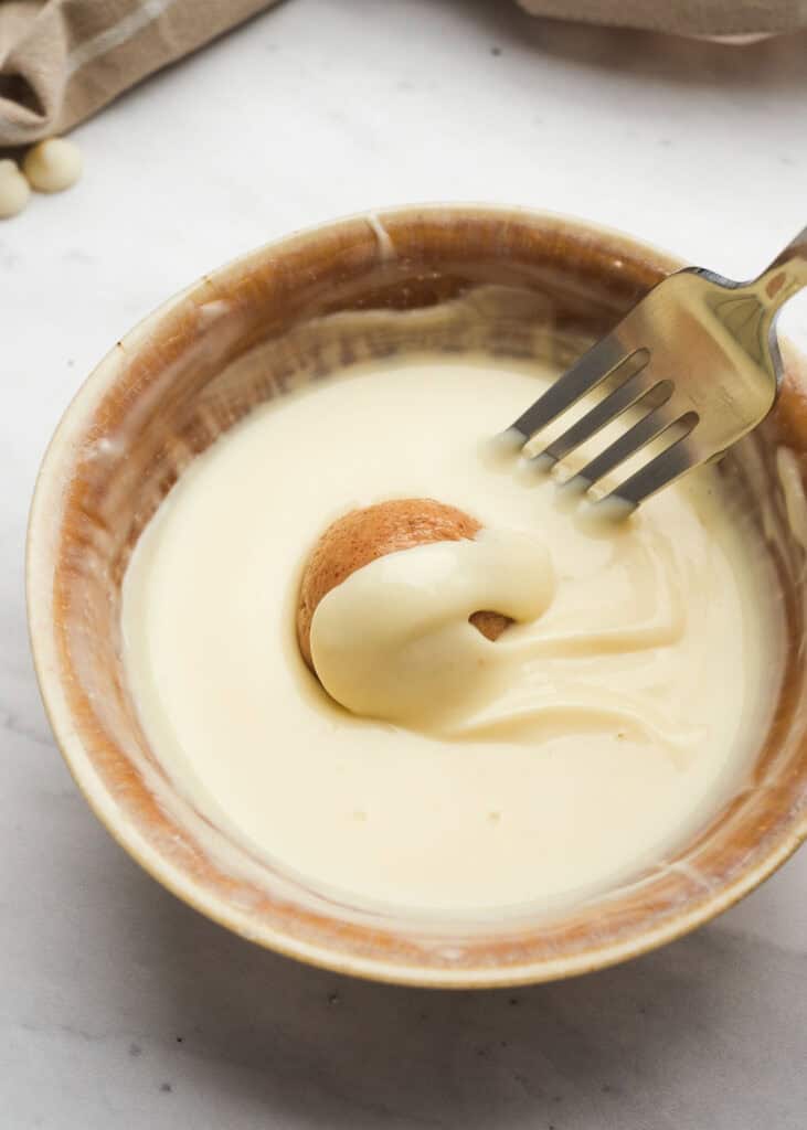 almond butter truffle being dipped in white chocolate coating 