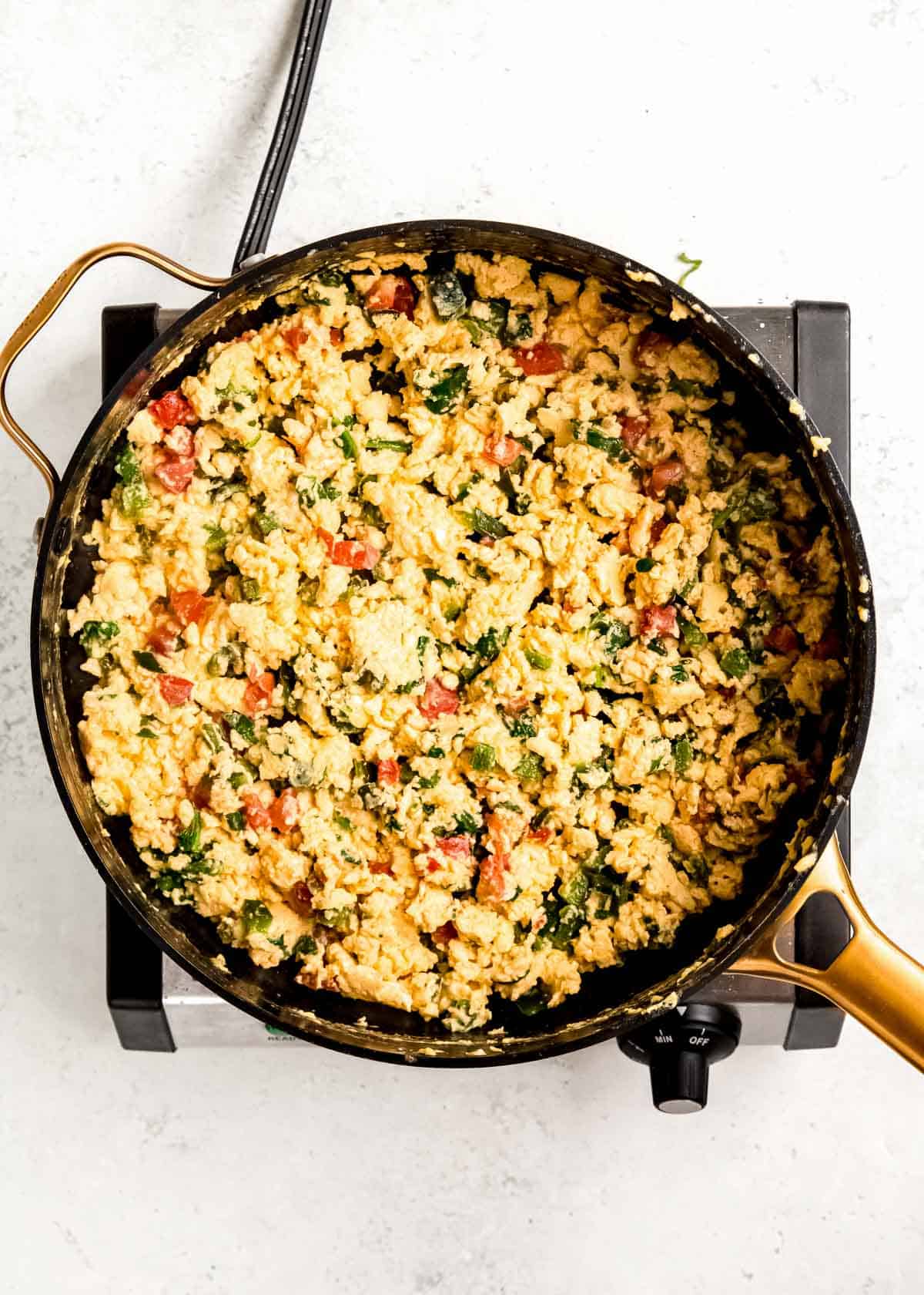 eggs and veggies being scrambled in black skillet