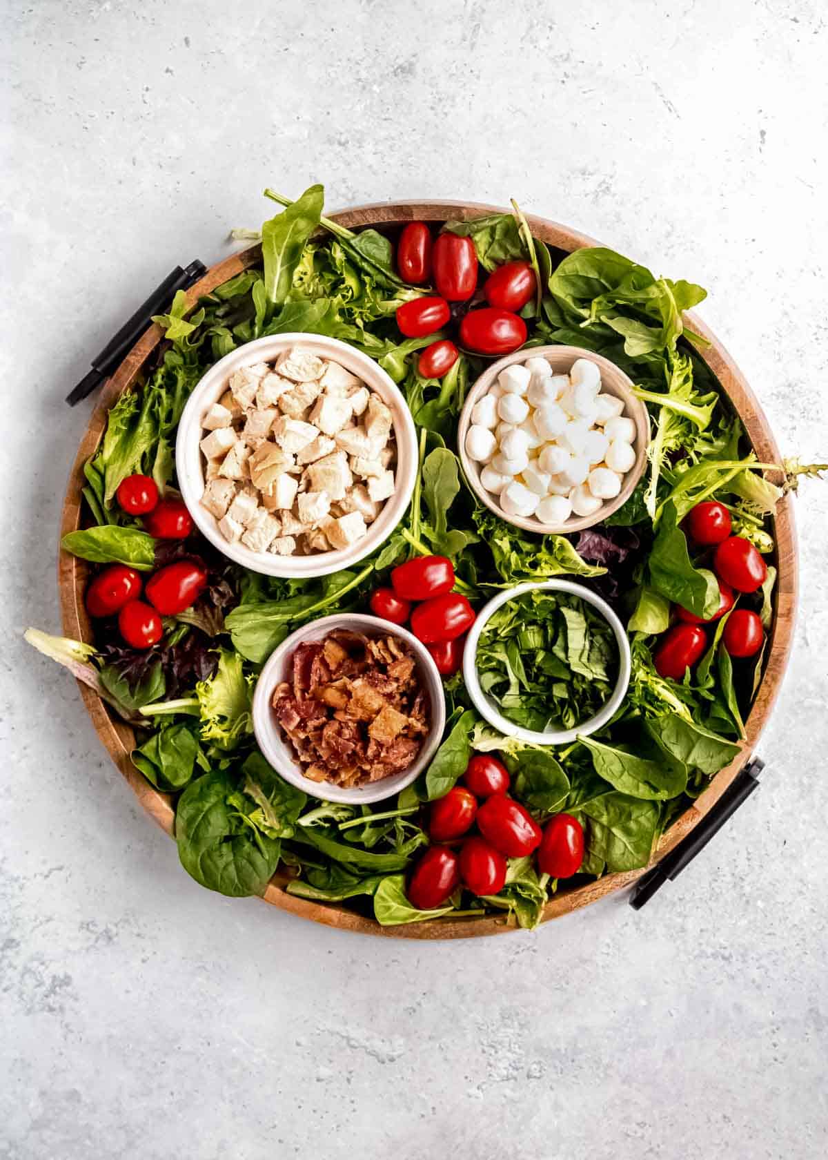 overhead image of chicken, bacon, mozzarella, mixed greens, and tomatoes on wooden cutting board