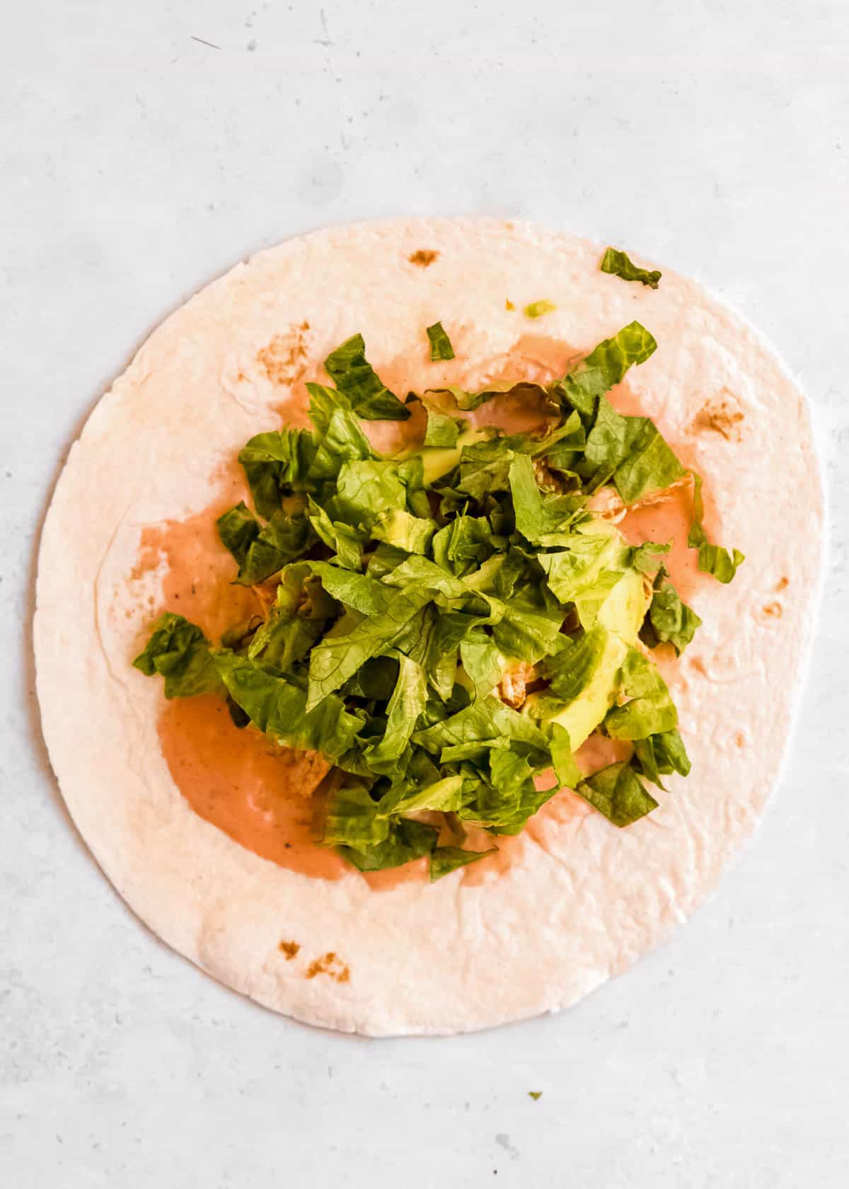 lettuce and avocado being added to buffalo chicken wrap