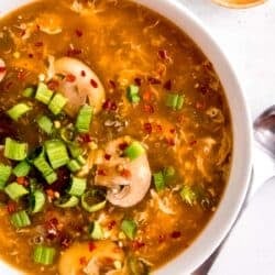 close up overhead image of hot and sour soup in white bowl and spoon sitting on white table