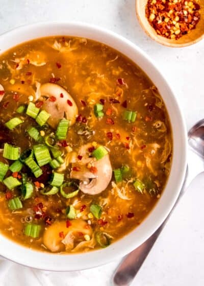 close up overhead image of hot and sour soup in white bowl and spoon sitting on white table